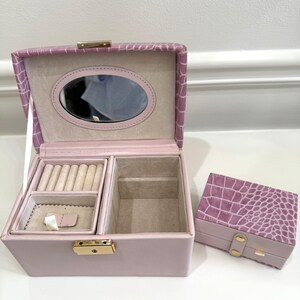 May include: A light purple jewelry box with a crocodile-embossed texture, featuring an open lid with an oval mirror, a beige velvet-lined interior with ring rolls and compartments, and a smaller matching closed jewelry box with gold-tone hardware.