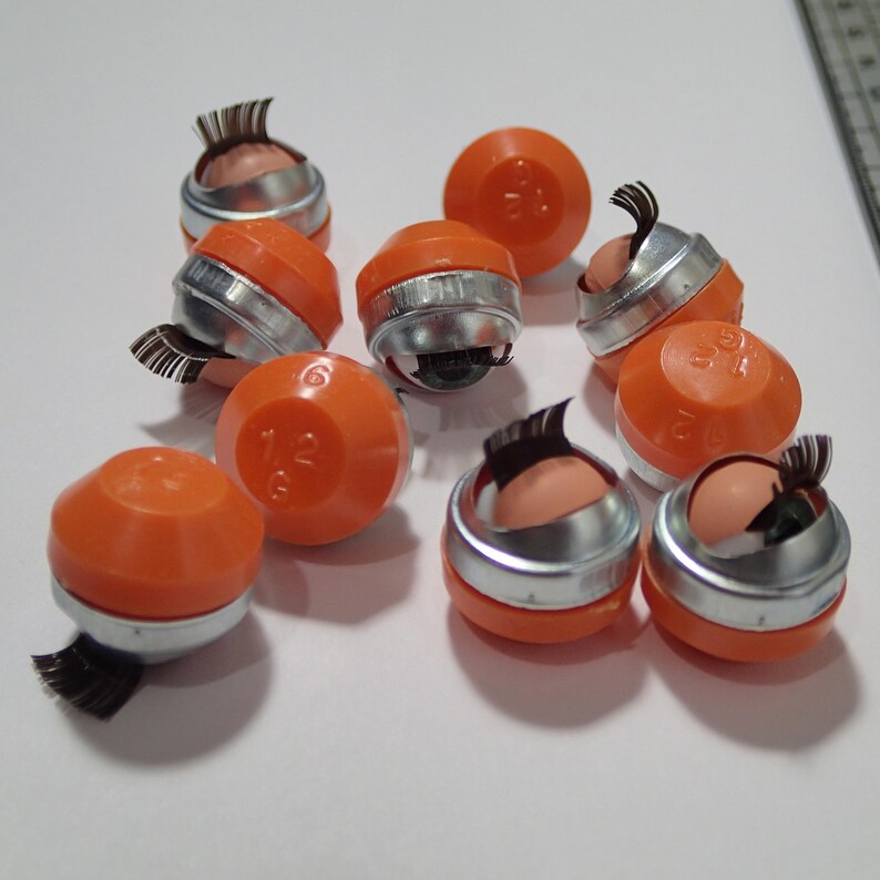 May include: Ten orange and silver eyelash applicators with black lashes. The applicators have a round shape and a silver band around the middle. The lashes are attached to the top of the applicator.