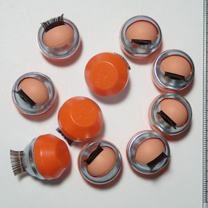 May include: Ten orange and silver containers with a small, black, eyelash-like object inside each one.