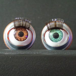 May include: Two large, round, plastic doll eyes with black eyelashes. One eye is brown with a purple iris and the other is green with a black iris.