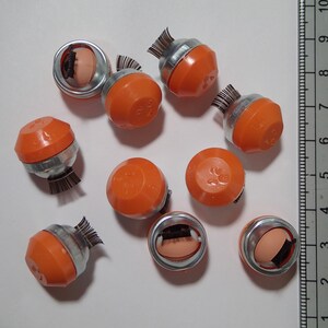 May include: Ten orange and silver round objects with black bristles. The objects have numbers printed on them, such as "1/2" and "1/4".