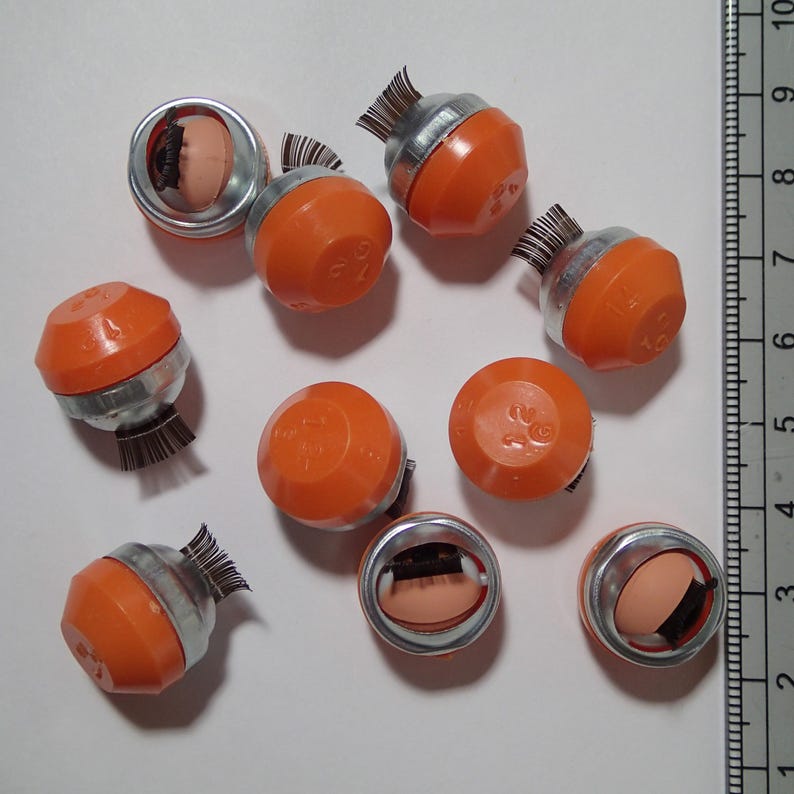 May include: Ten orange and silver round objects with black bristles. The objects have numbers printed on them, such as "1/2" and "1/4".