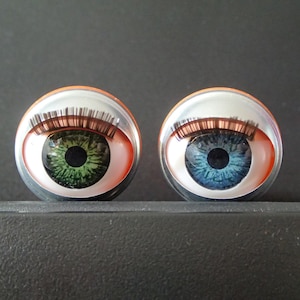 May include: Two large, round, googly eyes with silver rims and orange backs. The left eye has green irises and the right eye has blue irises.