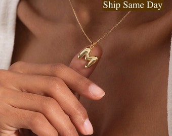 May include: A gold chain necklace with a chunky, gold letter 'M' pendant.