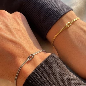 May include: Two simple bracelets with a knot design. One bracelet is gold and the other is silver.