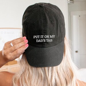May include: A black baseball cap with white embroidered text that reads "PUT IT ON MY DAD'S TAB".