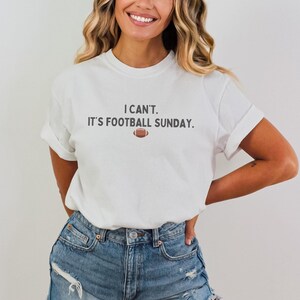 K&ouml;nnte beinhalten: Wei&szlig;es T-Shirt mit hochgekrempelten &Auml;rmeln und dem Text "I CAN'T. IT'S FOOTBALL SUNDAY." sowie einer Football-Grafik. Ein l&auml;ssiges Shirt, geeignet f&uuml;r den Spieltag oder den Alltag.