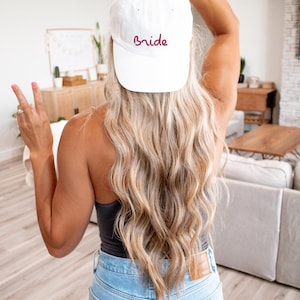 May include: A white baseball cap with the word "Bride" embroidered in burgundy on the front.