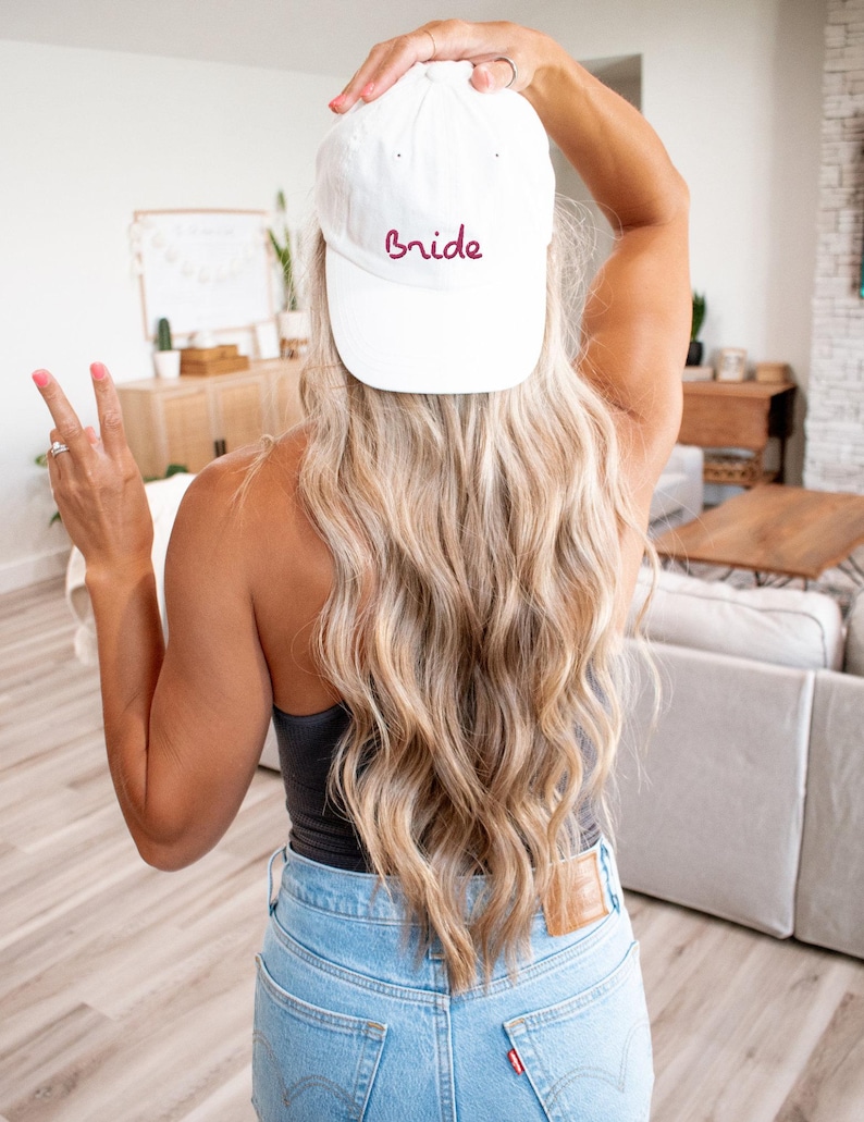 May include: A white baseball cap with the word "Bride" embroidered in burgundy on the front.