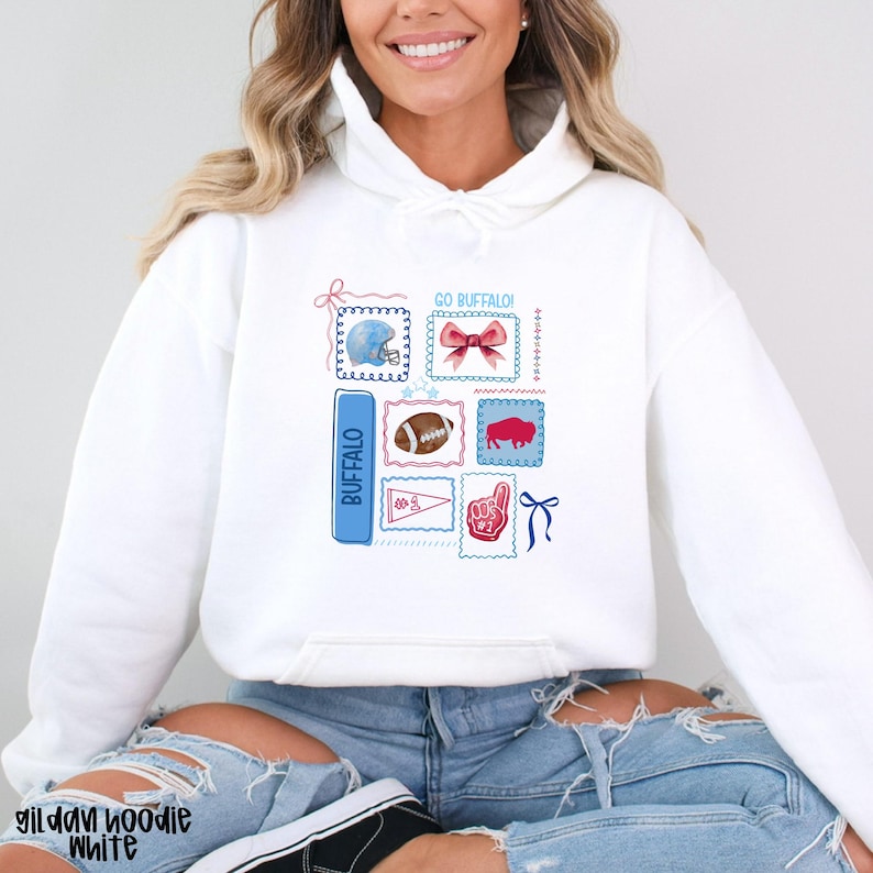 May include: White hoodie featuring a collection of Buffalo-themed graphics. The design includes a football, a helmet, a ribbon, and the word "Buffalo" in blue. The hoodie also has the text "GO BUFFALO!" and a foam finger graphic.