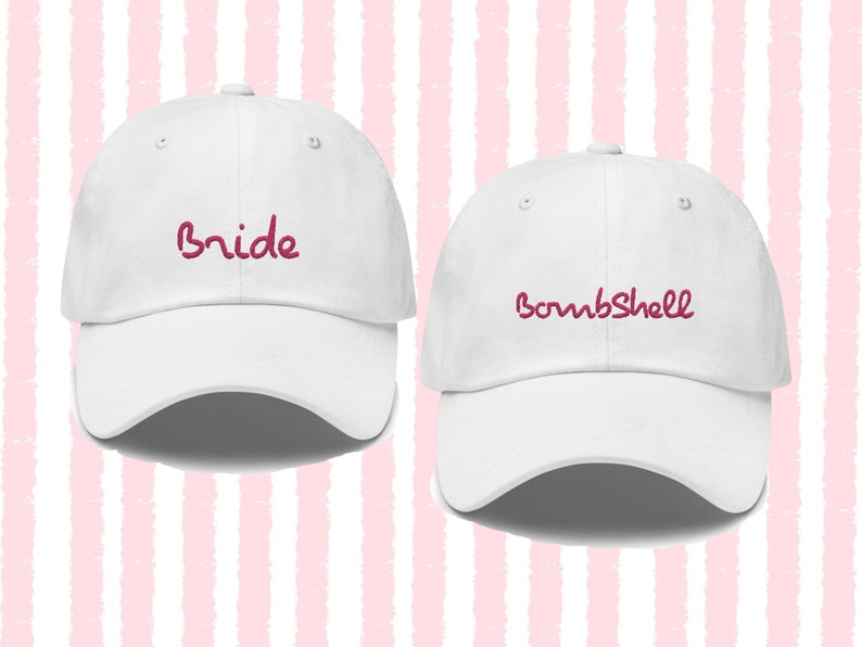 May include: Two white baseball caps with pink embroidered text. The left cap says "Bride" and the right cap says "Bombshell".
