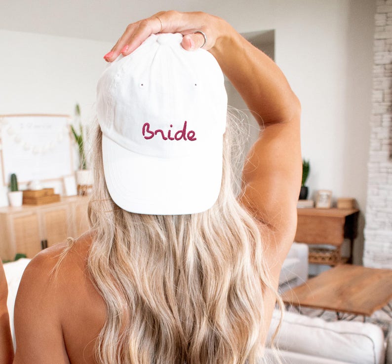 May include: White baseball cap with the word "bride" embroidered in burgundy on the front.
