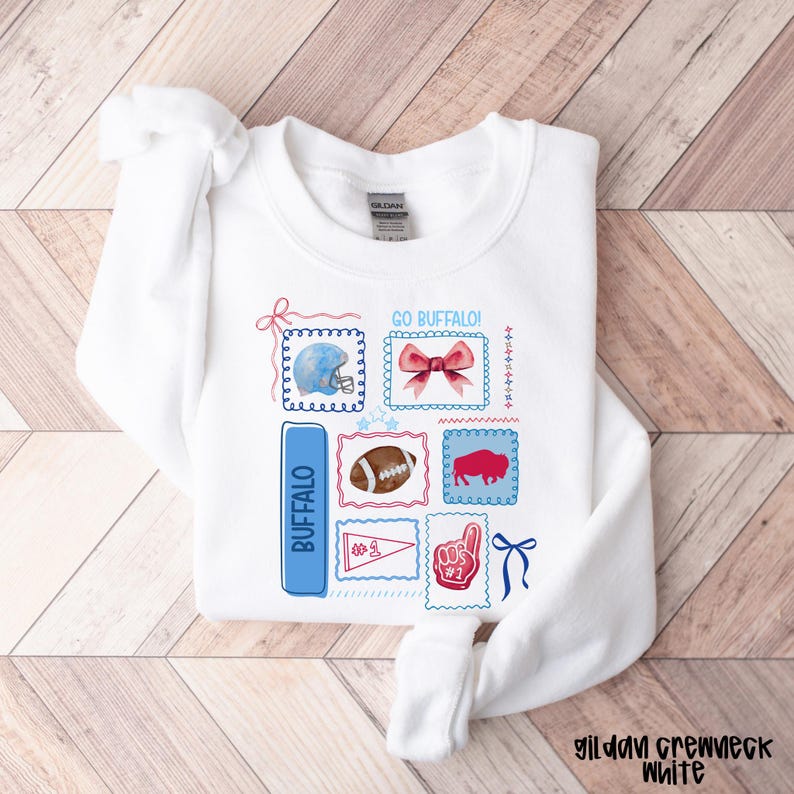 May include: White crewneck sweatshirt with a colorful Buffalo-themed design. The design includes a blue football helmet, a football, a red buffalo, and the text "GO BUFFALO!" and "BUFFALO".