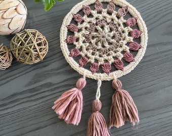May include: A crocheted dream catcher with a brown and pink mandala design and three pink tassels.