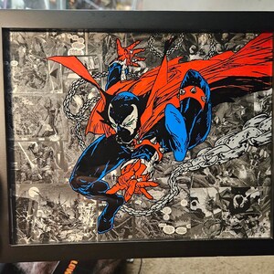 May include: Framed artwork featuring a comic book character, Spawn, in a dynamic pose with a red cape and chains. The artwork is made of a collage of comic book panels.