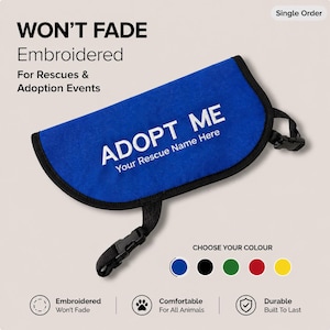 Puede incluir: Accesorio de adopción para mascotas bordado en azul con el texto "ADOPT ME" y "Your Rescue Name Here". Tiene un ribete negro y correas ajustables. También se ve el texto "WON'T FADE" y "Embroidered".