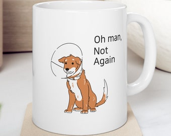 May include: White ceramic coffee mug with a brown dog wearing a cone of shame. The text on the mug reads "Oh man, Not Again".