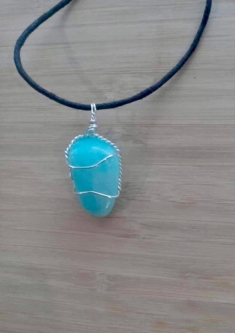 May include: A turquoise gemstone pendant wrapped in silver wire, hanging from a black cord necklace.