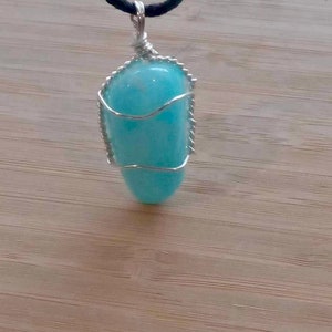 May include: A light blue gemstone pendant wrapped in silver wire, hanging from a black cord.