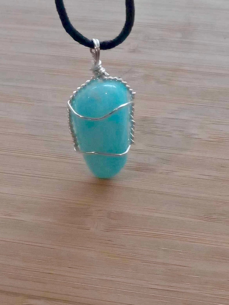 May include: A light blue gemstone pendant wrapped in silver wire, hanging from a black cord.