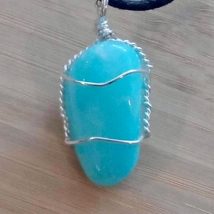 May include: A turquoise gemstone pendant wrapped in silver wire, hanging from a black cord.