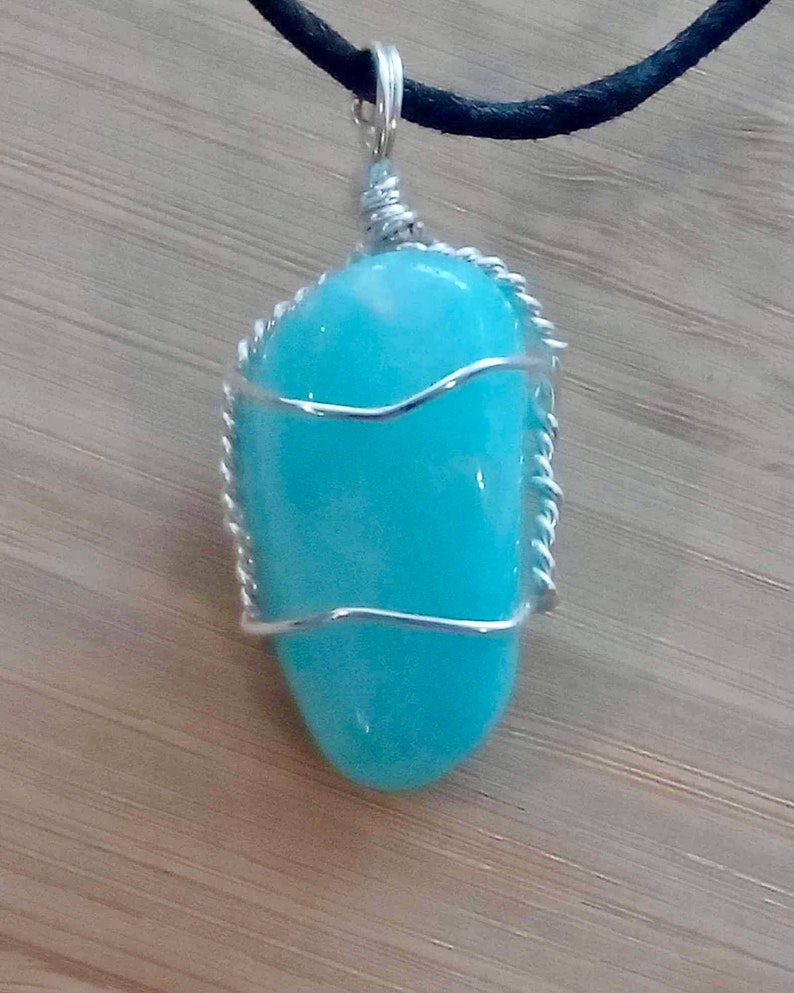 May include: A turquoise gemstone pendant wrapped in silver wire, hanging from a black cord.
