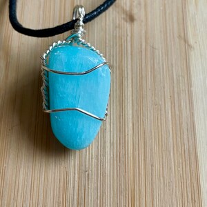 May include: A light blue gemstone pendant wrapped in silver wire, hanging from a black leather cord.