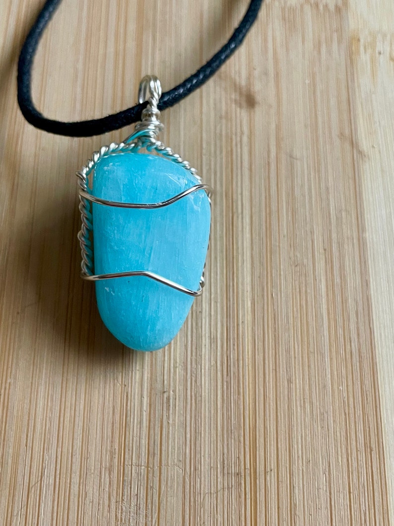 May include: A light blue gemstone pendant wrapped in silver wire, hanging from a black leather cord.