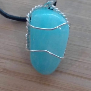 May include: A turquoise gemstone pendant wrapped in silver wire, hanging from a black leather cord.