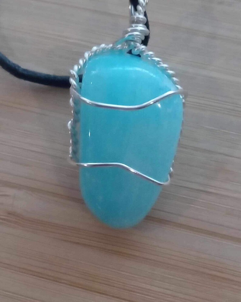 May include: A turquoise gemstone pendant wrapped in silver wire, hanging from a black leather cord.
