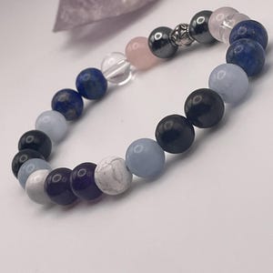 Puede incluir: Un brazalete de cuentas con una variedad de piedras, incluyendo amatista, cuarzo transparente, cuarzo rosa, ágata azul, lapislázuli y ónix negro. El brazalete tiene un cierre plateado.