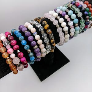 Puede incluir: Una colección de pulseras de cuentas de colores con detalles plateados. Las pulseras están hechas con varias piedras preciosas, incluyendo amatista, ojo de tigre, cuarzo rosa y cuarzo transparente.