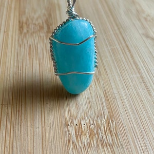 May include: A light blue aquamarine stone pendant wrapped in silver wire, hanging from a black cord.