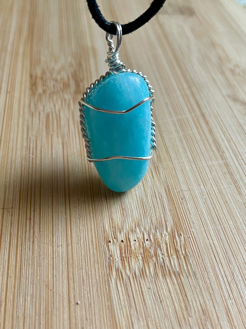 May include: A light blue aquamarine stone pendant wrapped in silver wire, hanging from a black cord.