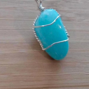 May include: A light blue gemstone pendant wrapped in silver wire, hanging from a black cord.