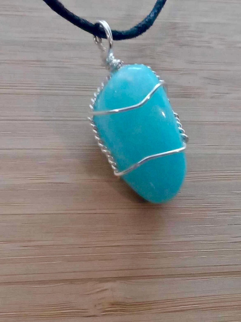 May include: A light blue gemstone pendant wrapped in silver wire, hanging from a black cord.