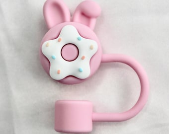 May include: Pink silicone phone holder with a donut design and bunny ears. The donut has white frosting and colorful sprinkles.