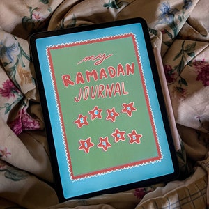May include: A digital tablet displaying a journal cover with the text "my Ramadan JOURNAL" in red script. The cover has a green background with red stars and numbers. A stylus rests on the side of the tablet, which is on a floral patterned fabric.