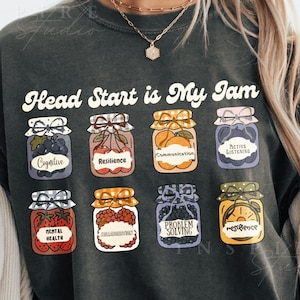 May include: Dark gray sweatshirt with the text "Head Start is My Jam" in white script. The shirt features colorful illustrations of jam jars, each labeled with a positive concept like "Resilience" and "Mental Health".