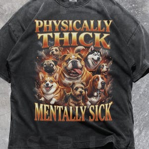 May include: Dark gray t-shirt featuring a graphic of various dog breeds with the text "PHYSICALLY THICK MENTALLY SICK" in orange and gold lettering. The shirt has a vintage, distressed look.