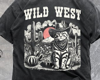 May include: Black t-shirt with a Wild West graphic. The design features a cat wearing a cowboy hat and bandana, set against a desert landscape with cacti and a red sun. The text "WILD WEST" is printed above the graphic.