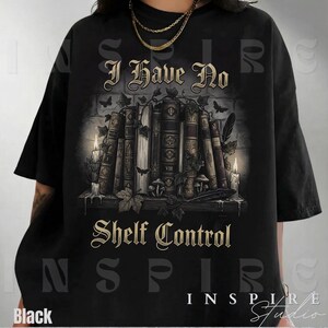 May include: Black t-shirt with the text "I Have No Shelf Control" in gold lettering. The graphic features a stack of old books, candles, and foliage. The word "Black" is printed at the bottom left.