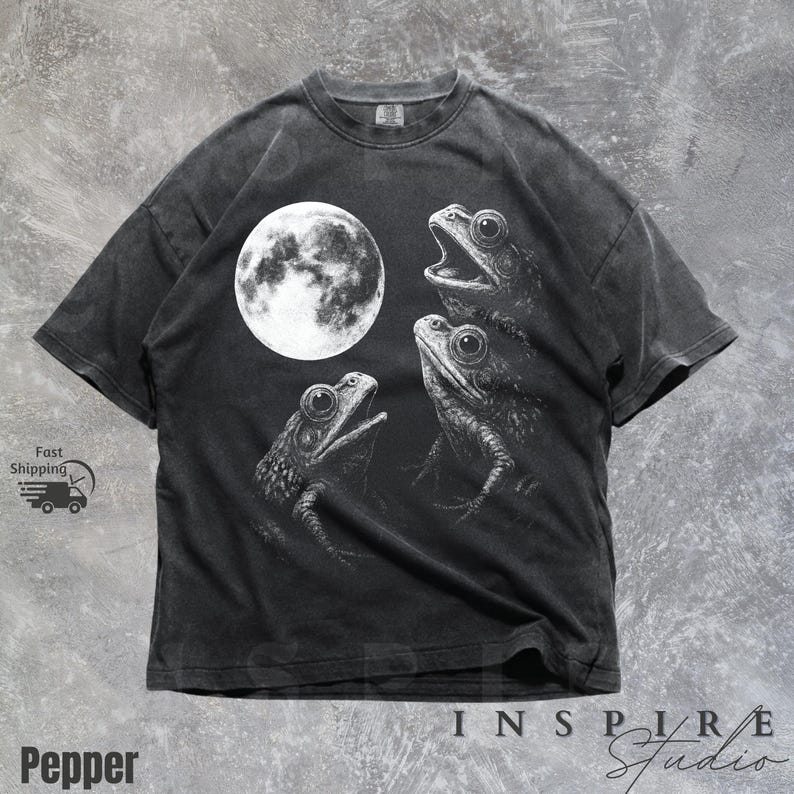 K&ouml;nnte beinhalten: Dunkelgraues T-Shirt mit einer wei&szlig;en Illustration von drei Fr&ouml;schen und einem Vollmond. Das detaillierte Design erzeugt einen starken Kontrast. Das T-Shirt hat einen Vintage-Look.
