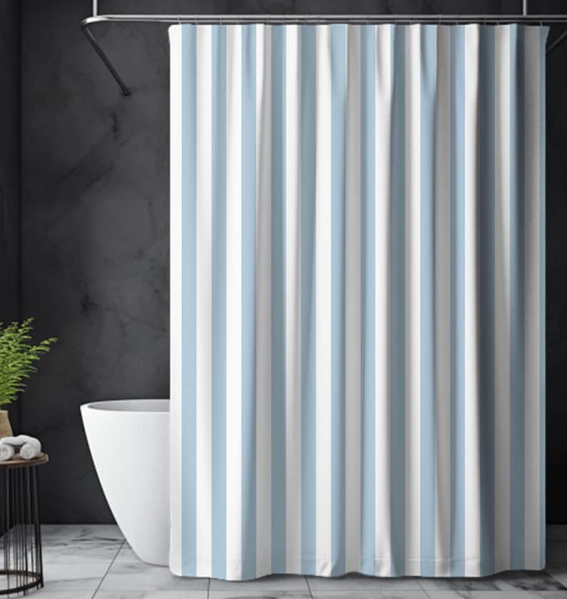 May include: A shower curtain with vertical stripes in light blue and white. The curtain hangs in front of a white bathtub, with a dark gray wall in the background. The curtain is made of a soft, opaque material.