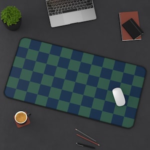 May include: A rectangular desk mat with a checkered pattern in navy blue and green. A white computer mouse sits on the mat. Other items on the desk include a laptop, a small potted plant, a notebook, a cup of coffee, and writing utensils.