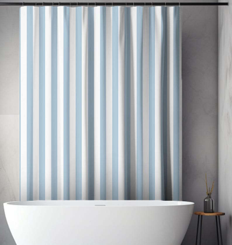 May include: A shower curtain with vertical stripes in light blue and white. The curtain hangs from a black rod above a white bathtub. The bathroom has a minimalist design with a neutral color palette.