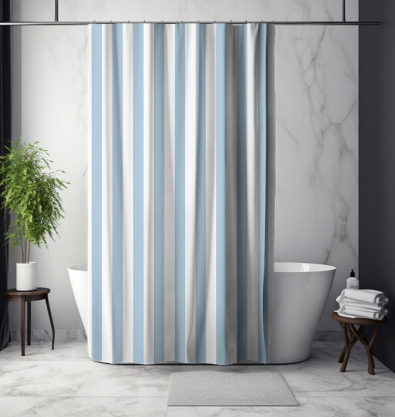 May include: A blue, white, and gray striped shower curtain hangs in front of a white bathtub. The curtain is the focal point, with vertical stripes. A small gray bath mat sits on the floor. A small wooden table holds a stack of white towels.