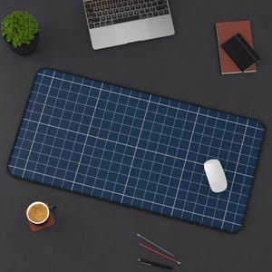 May include: A navy blue desk mat with a white grid pattern, a white computer mouse, and a laptop. A small potted plant, a notebook, a pen, and a cup of coffee are also on the dark surface.