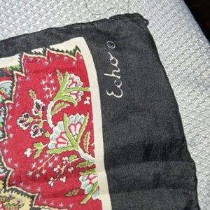 May include: A square scarf featuring a black border with the word Echo printed in white script. The central design displays a detailed floral pattern in shades of red, cream, light blue, and green, with intricate botanical motifs and fine line work.