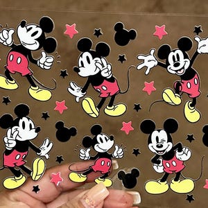 May include: A sheet of clear vinyl with multiple Mickey Mouse stickers. The stickers are red, black, and yellow. The stickers are arranged in a random pattern on the sheet.